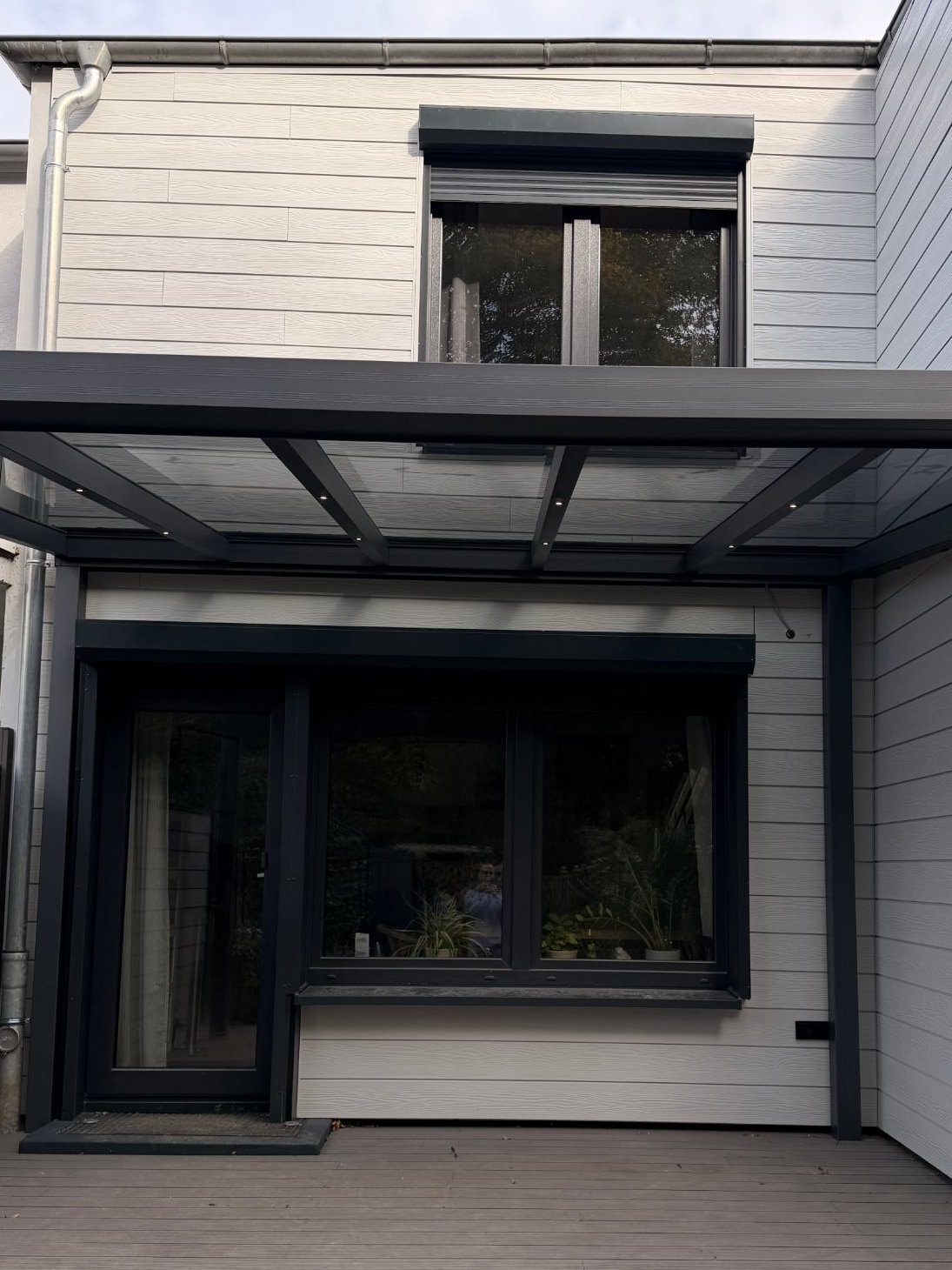 Gartenseite nachher: helle Fassadenverkleidung, Fenster und Tür in Anthrazit mit Rollläden, Terrassenüberdachung aus Glas und Terrassendielen