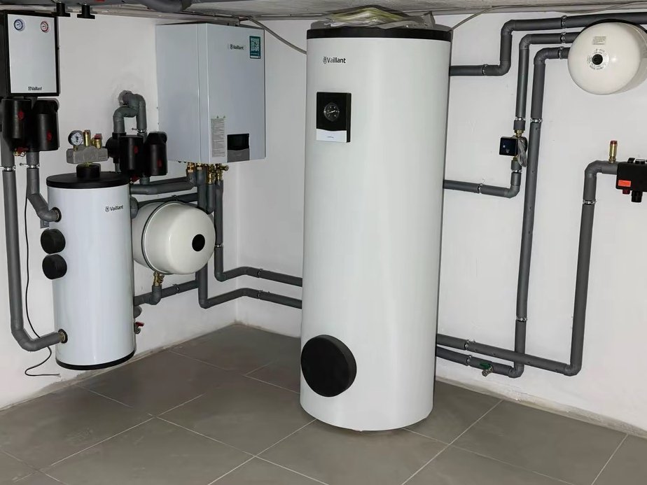 Heizraum nachher: Wärmepumpen-Innengerät, Warmwasserspeicher und Pufferspeicher mit grau gedämmten Rohrleitungen, weiße Wände und gefliester Boden