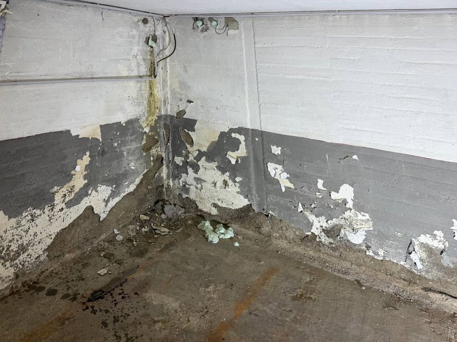 Kellerraum vorher: feuchte Wände mit abplatzender Farbe, offene Leitungen und Schutt auf dem Betonboden