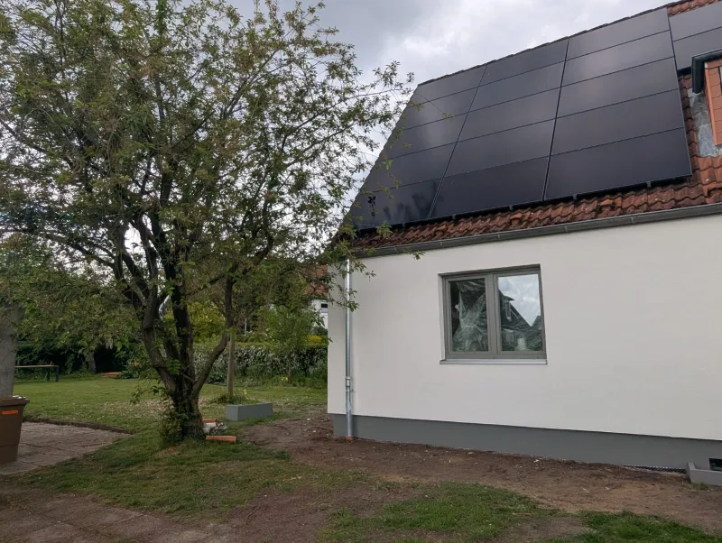 Steildach mit durchgehend schwarzen Photovoltaikmodulen über einer hell verputzten Fassade