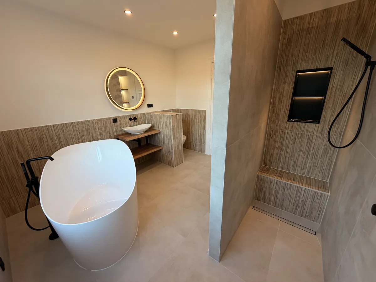 Saniertes Bad mit freistehender Badewanne, rundem beleuchtetem Spiegel und bodengleicher Dusche mit beleuchteter Nische